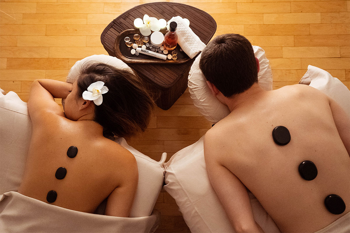 spa with woman and man with stones on their backs and cbd treatment on table with pillows