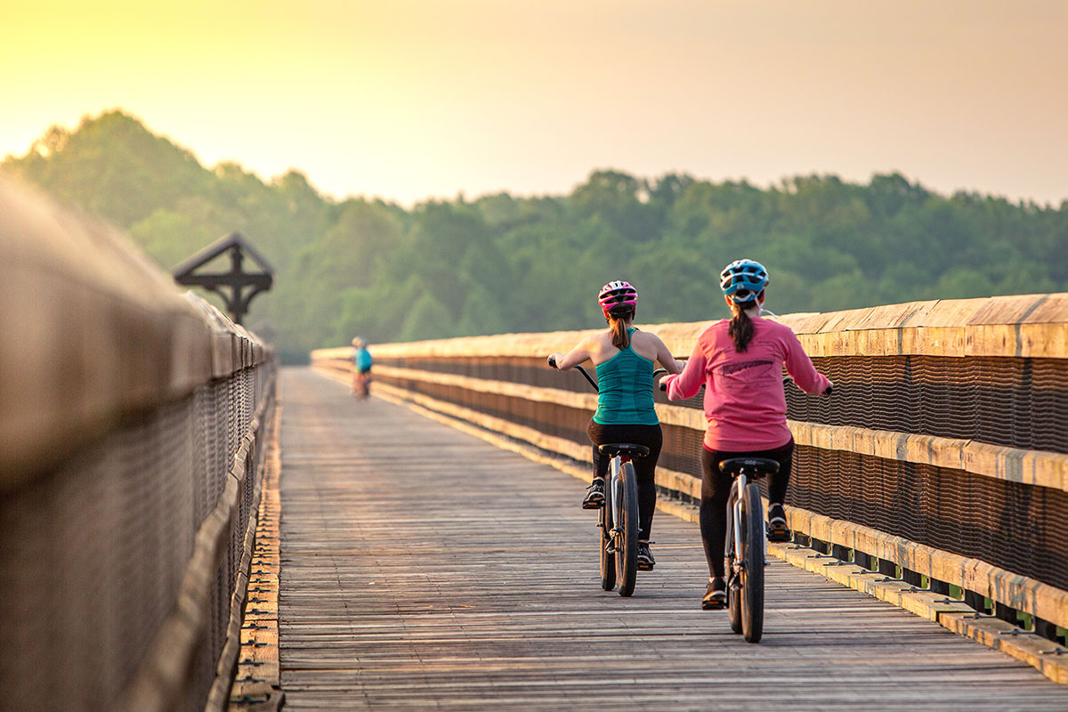 two women biking on bridge with sunset in background