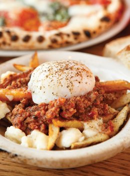 A poached egg sits atop an Italian version of poutine with Bolognese subbing for gravy. 