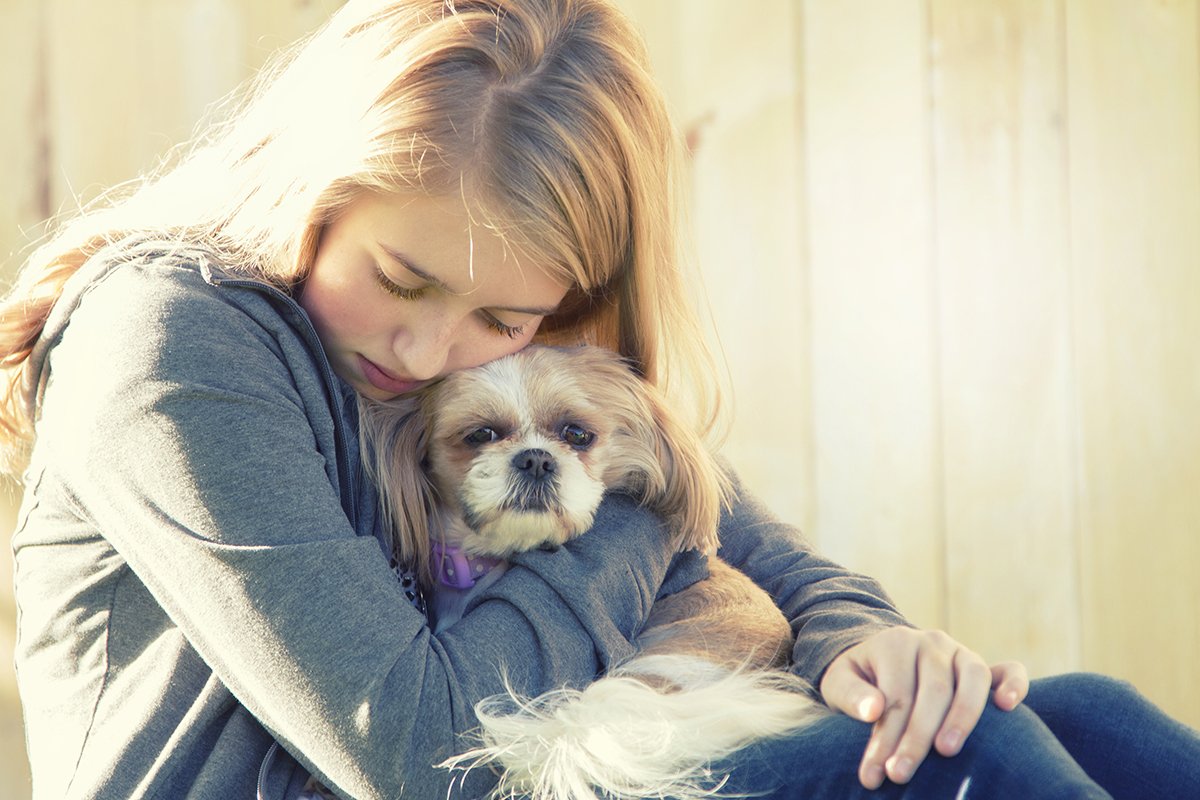 A sad or depressed teenage girl hugging a small dog