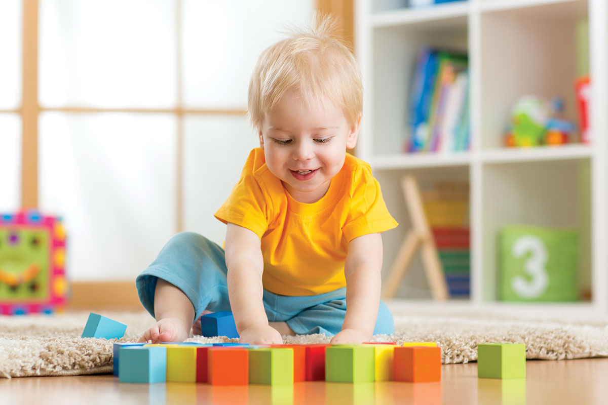 baby boy playing with colorful blocks in playroom