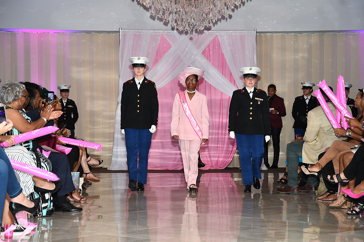 woman in pink with two soldiers walking on runway