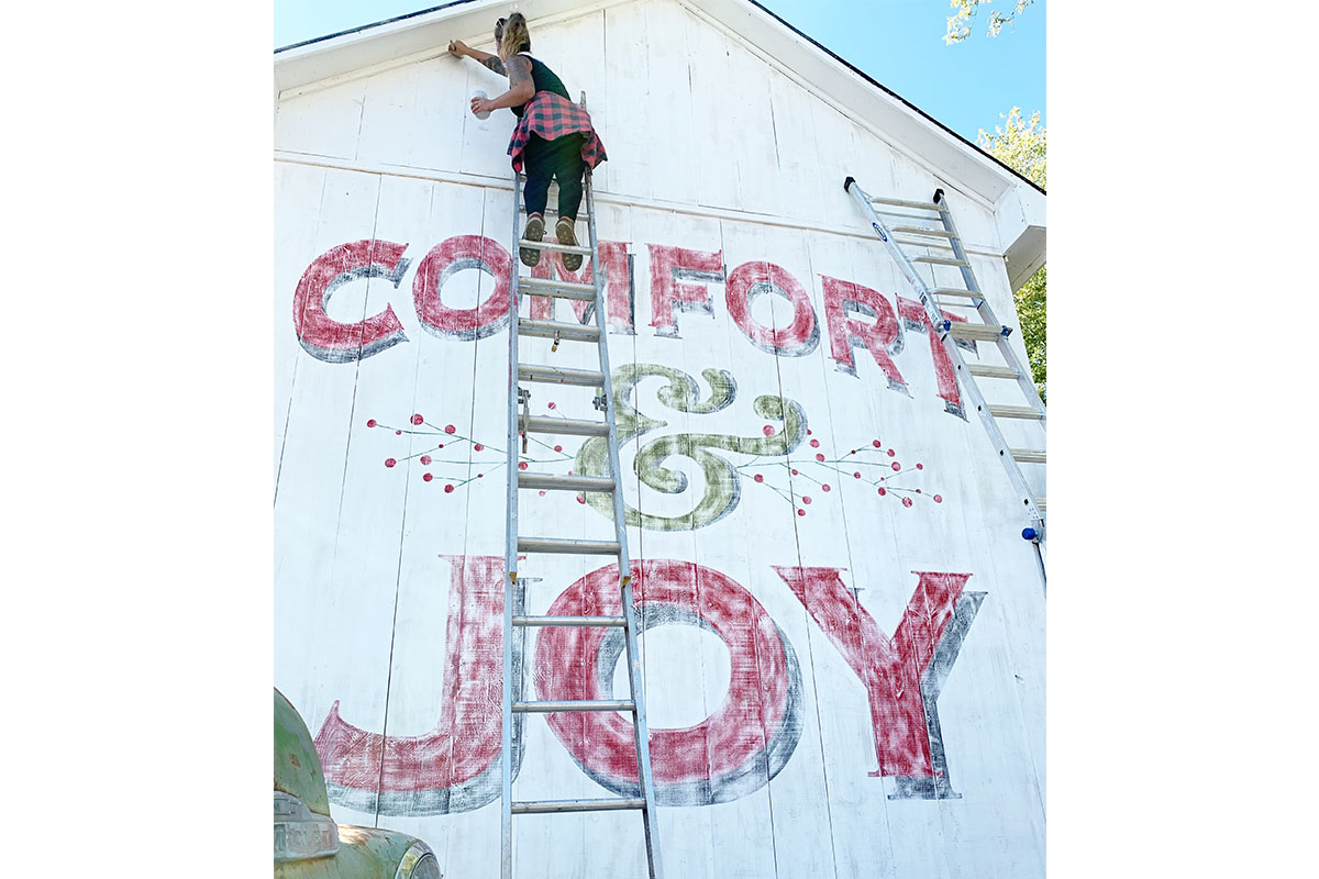 woman painting comfort & joy mural on barn