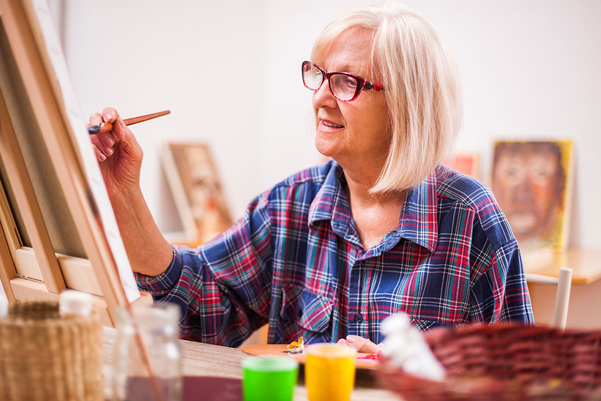 senior woman painting on canvas and easel