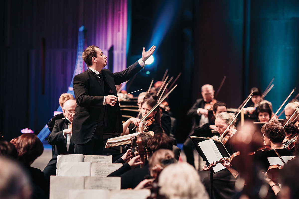 conductor leading orchestra with purple and blue background