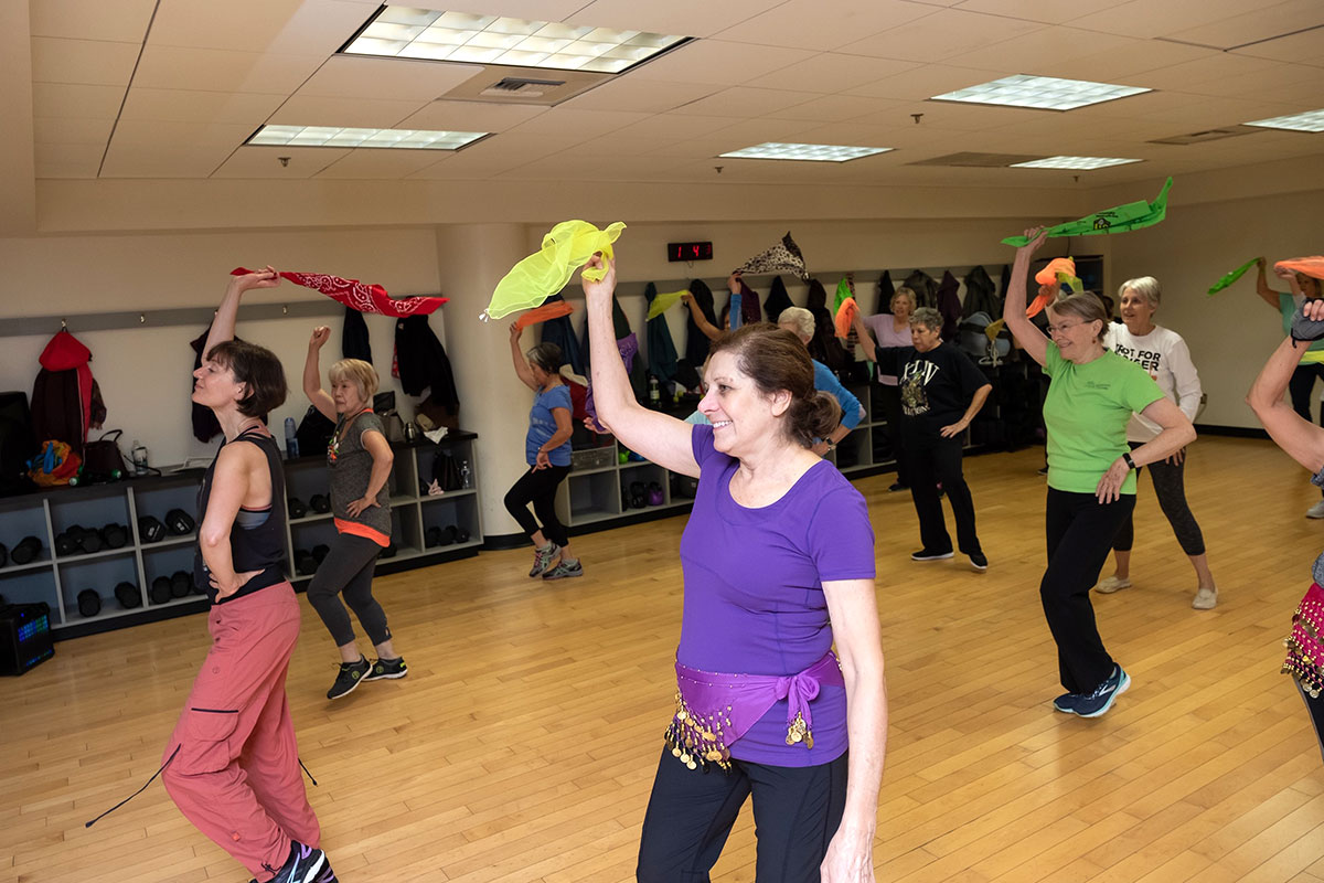 women in workout room with colorful bandanas above head
