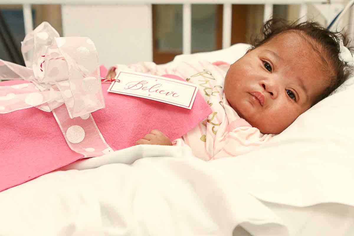 a baby at the nicu at children's national wrapped in a pink blanket and bow with the word believe on the tag