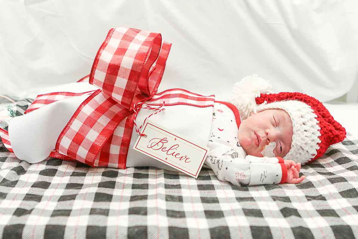 a baby at a holiday photo shoot wrapped in a red plaid bow