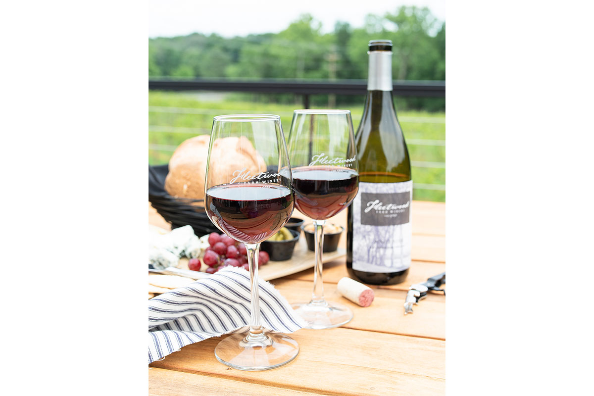 two glasses of red wine on wooden table with bottle of fleetwood farm wine