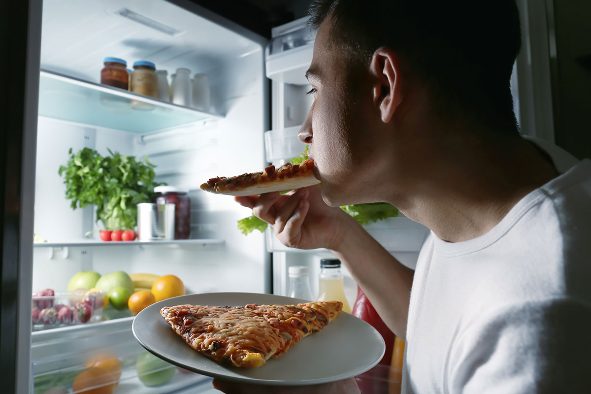 man eating pizza out of fridge
