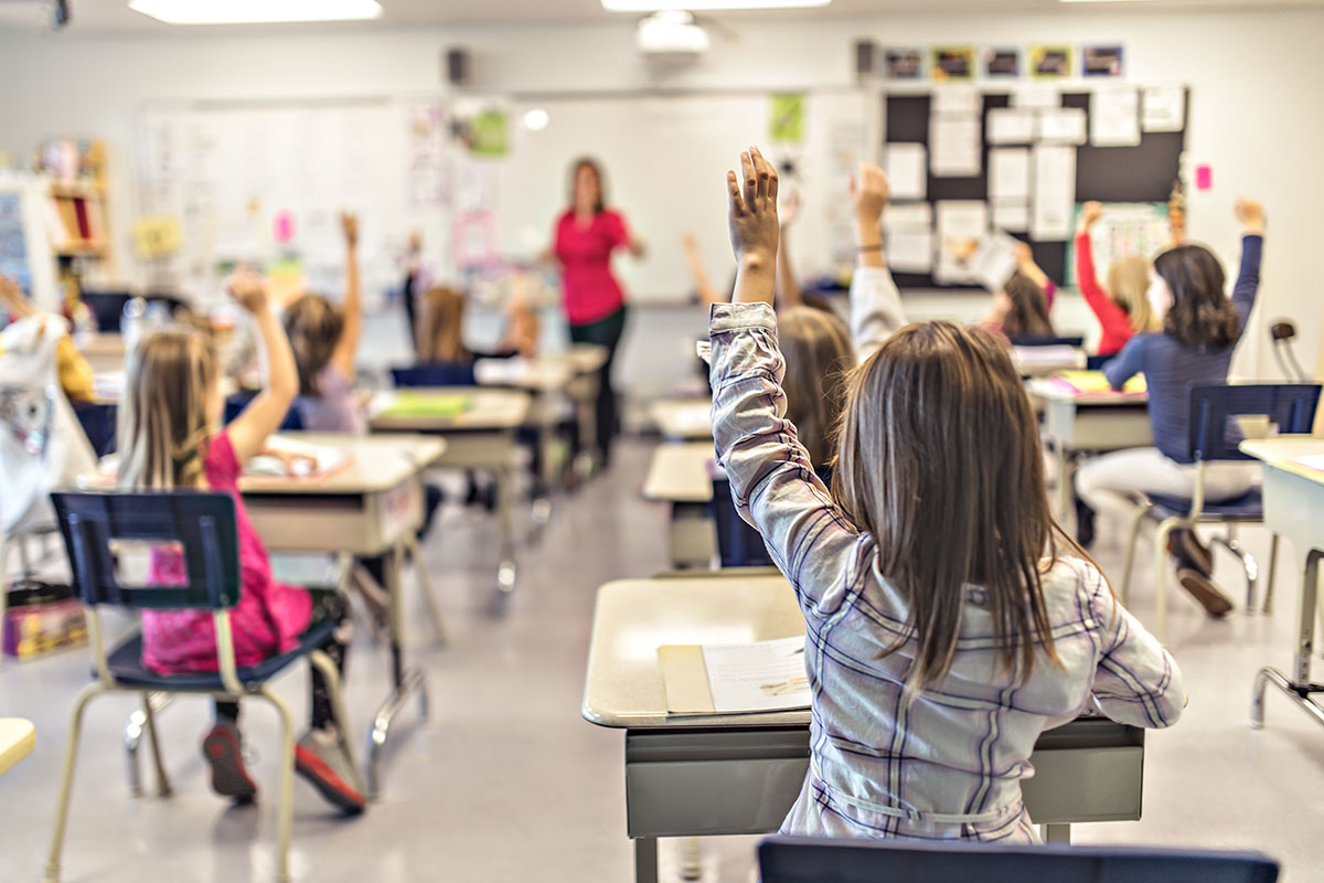 little girl raising her hand at the back of a classroom