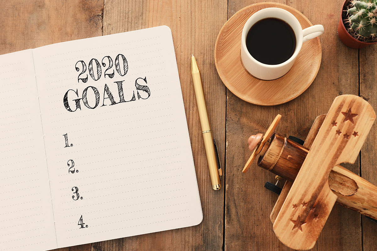 2020 goal notepad with coffee and wooden airplane on table