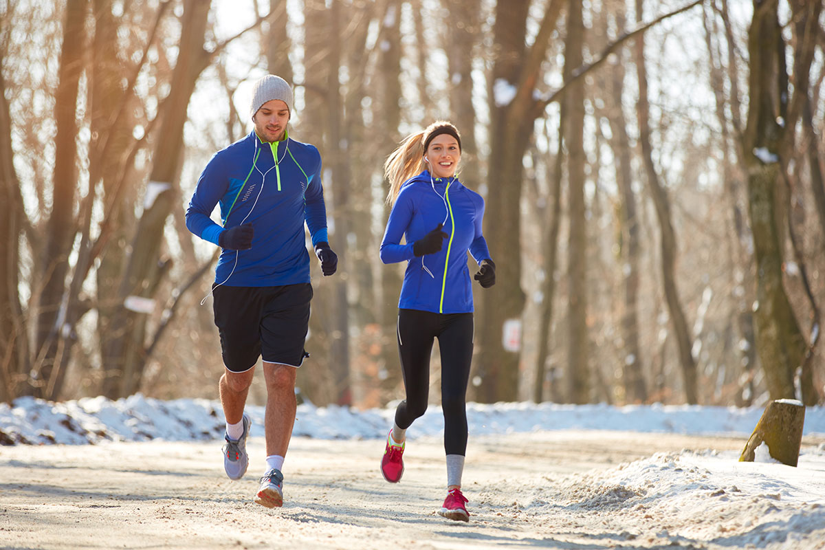 woman and man running in woods with snow wearing blue and black
