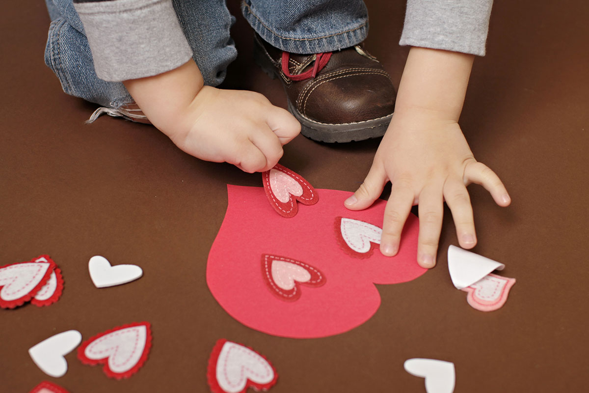 child putting paper hearts on red heart with glue