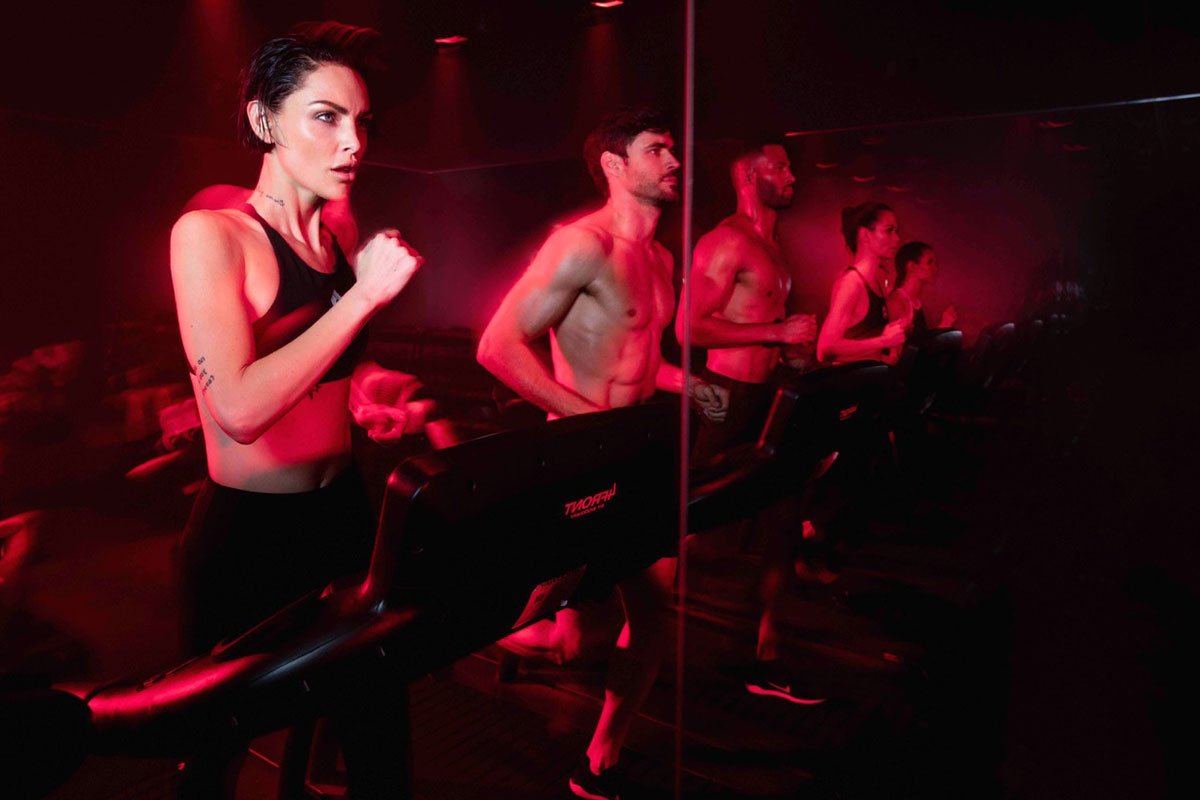 women and men running on a treadmill in front of a mirror with red lighting