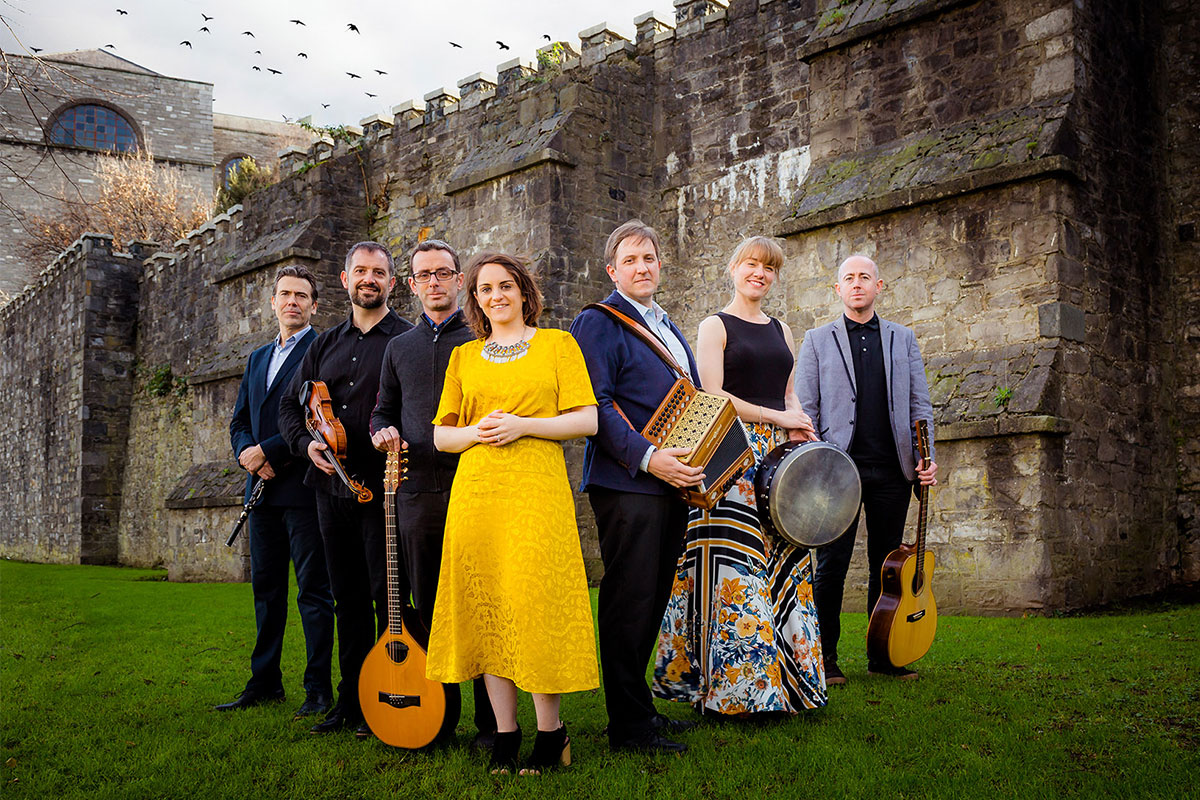 group of irish musicians in front of stone wall with yellow dress