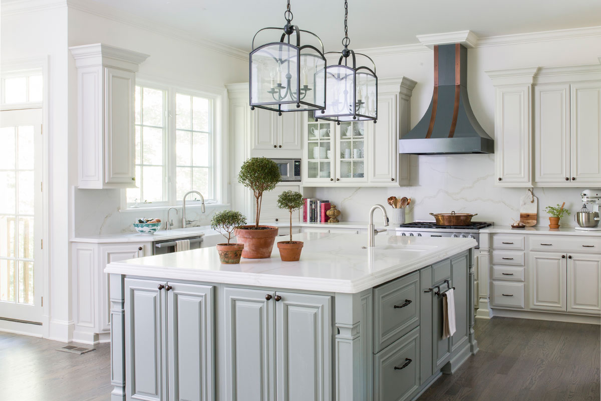 white kitchen with large island, black hanging lights and oven
