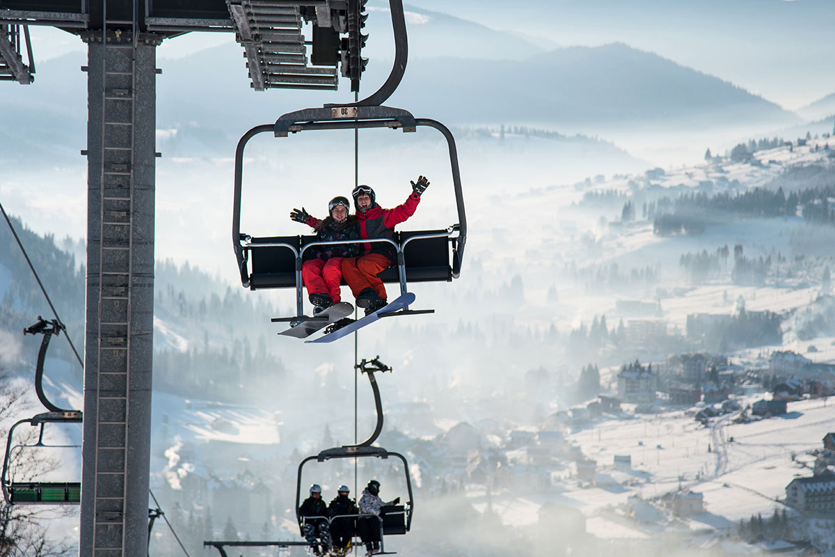 two people in red on a ski lift with a snow covered mountain in the background