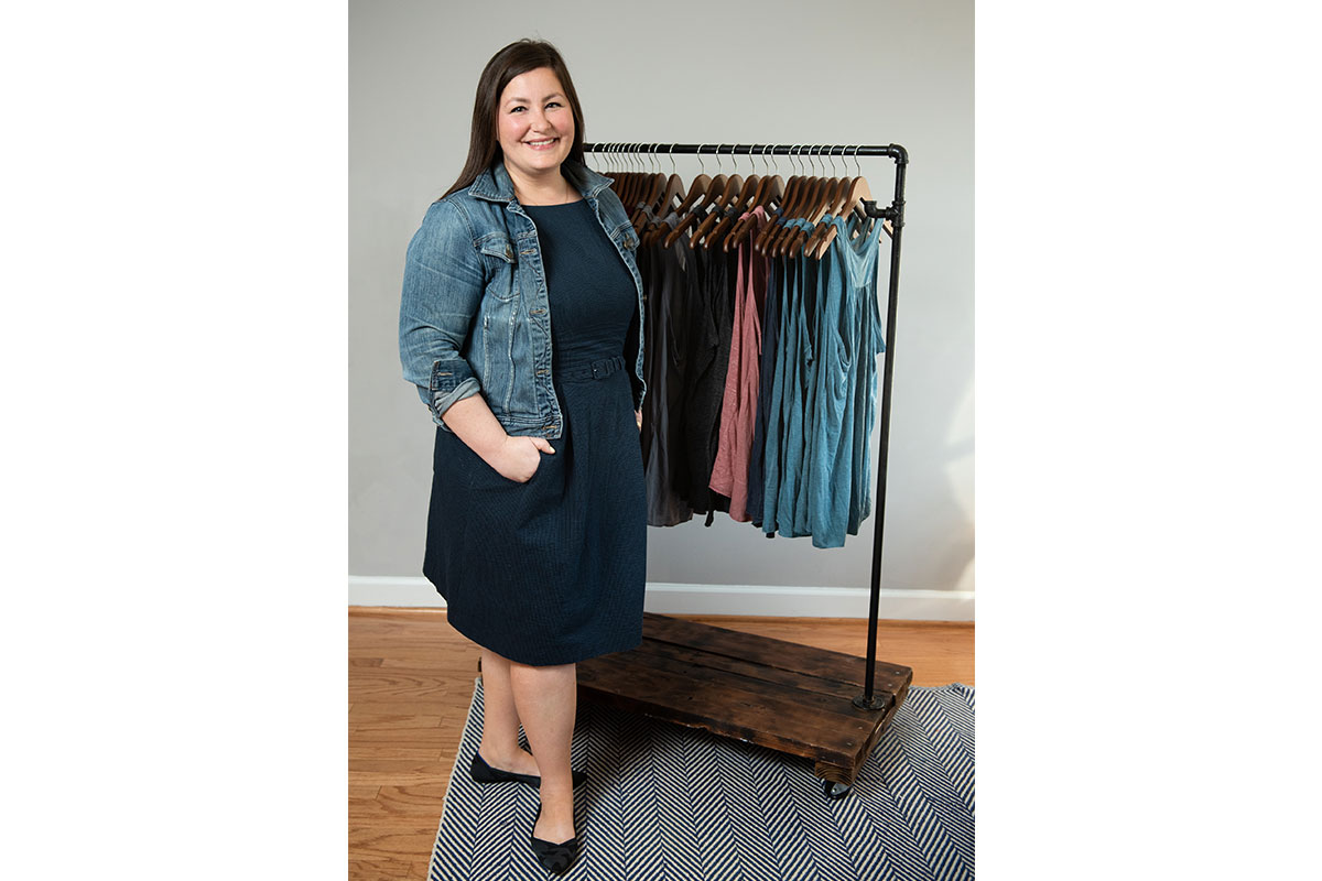 woman in black dress and jean jacket in front of rack