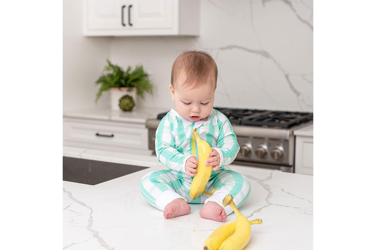 baby holding banana with light green onesie