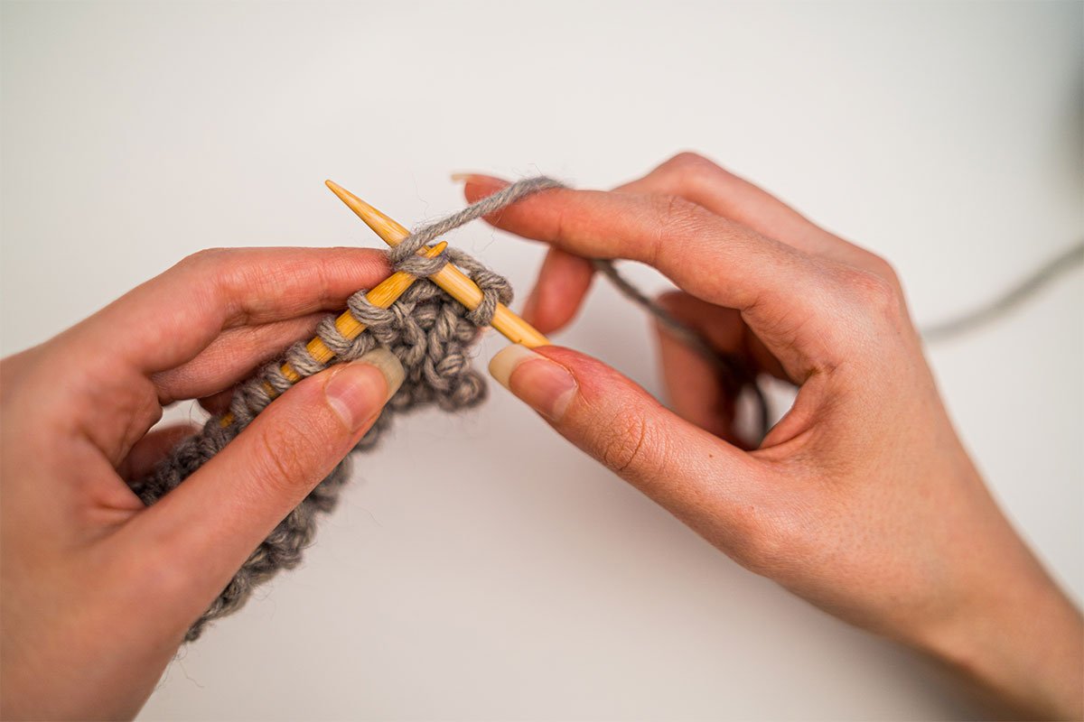 two hands knitting with gray yarn
