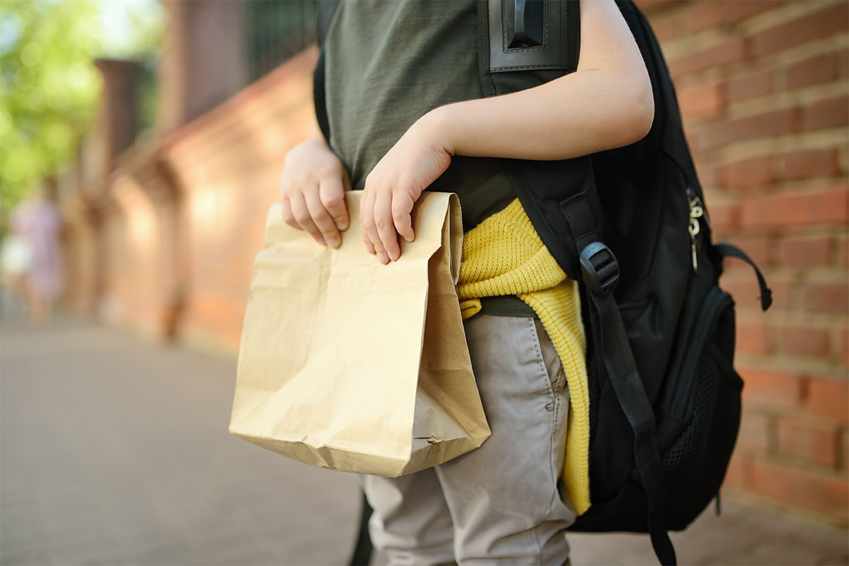 yougn child carrying backpack and paper bag school lunch