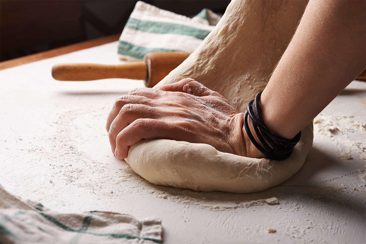 hands with bread dough on floured surface