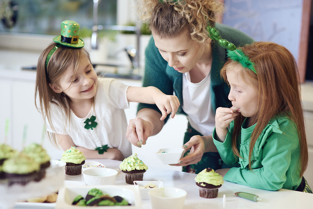 two little girls decorating cupcakes in green with mom