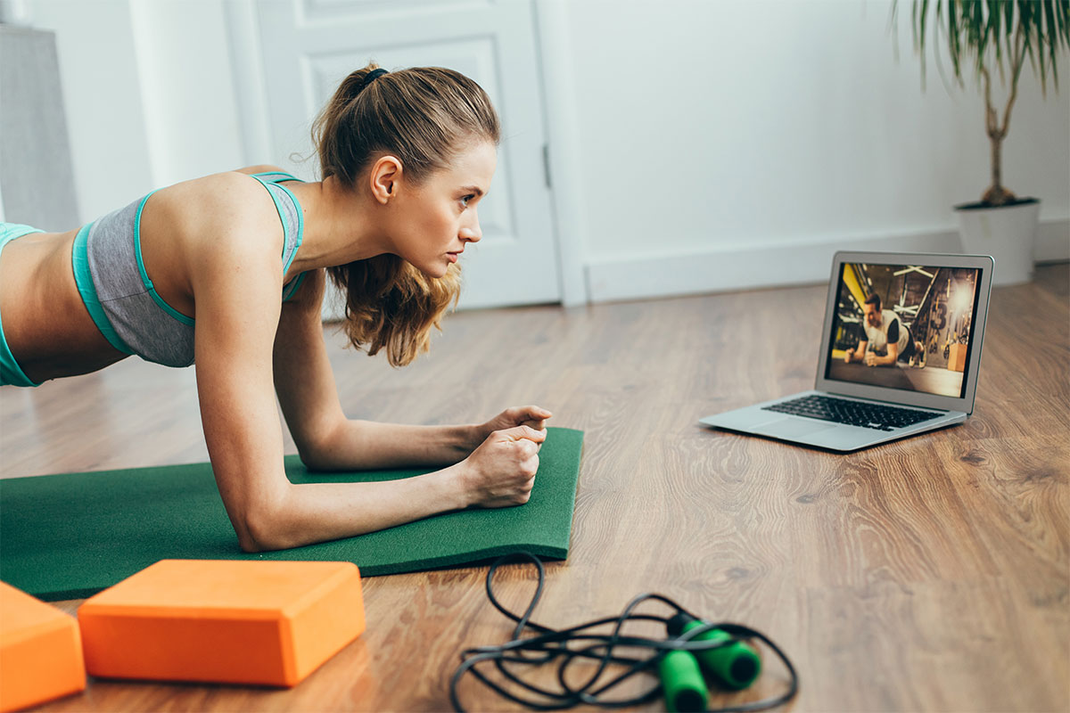 girl working out at home with laptop, orange block, yoga mat and jump rope