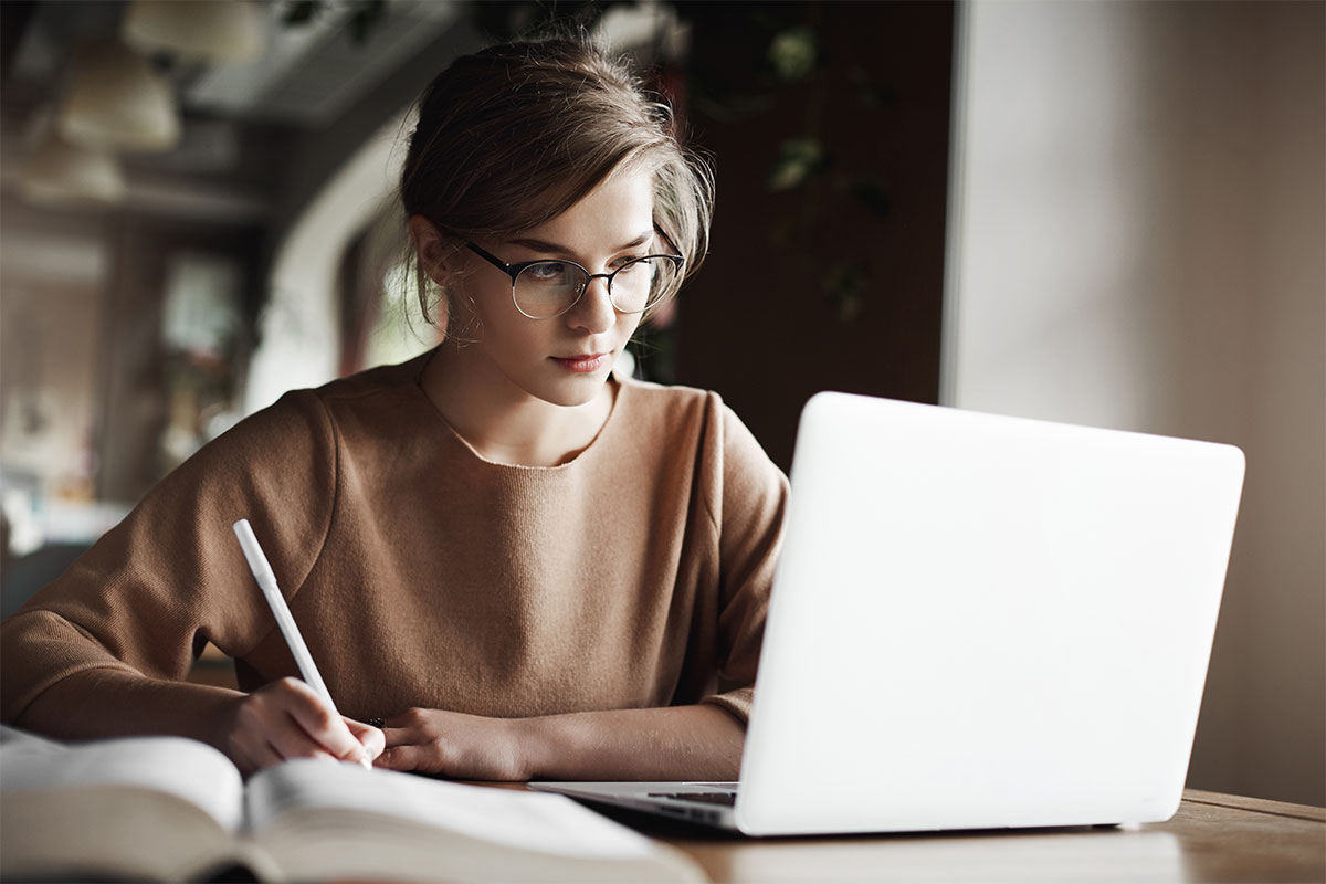 girl with glasses on silver laptop with pencil and book