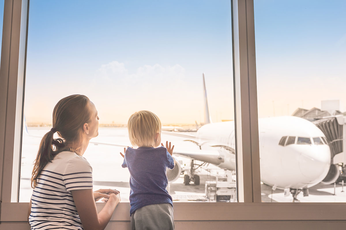 mother and child at airport looking out window at plane