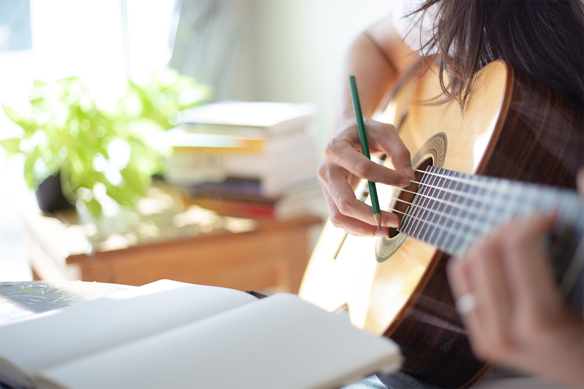 girl holding light brown guitar with green pencil and notebook