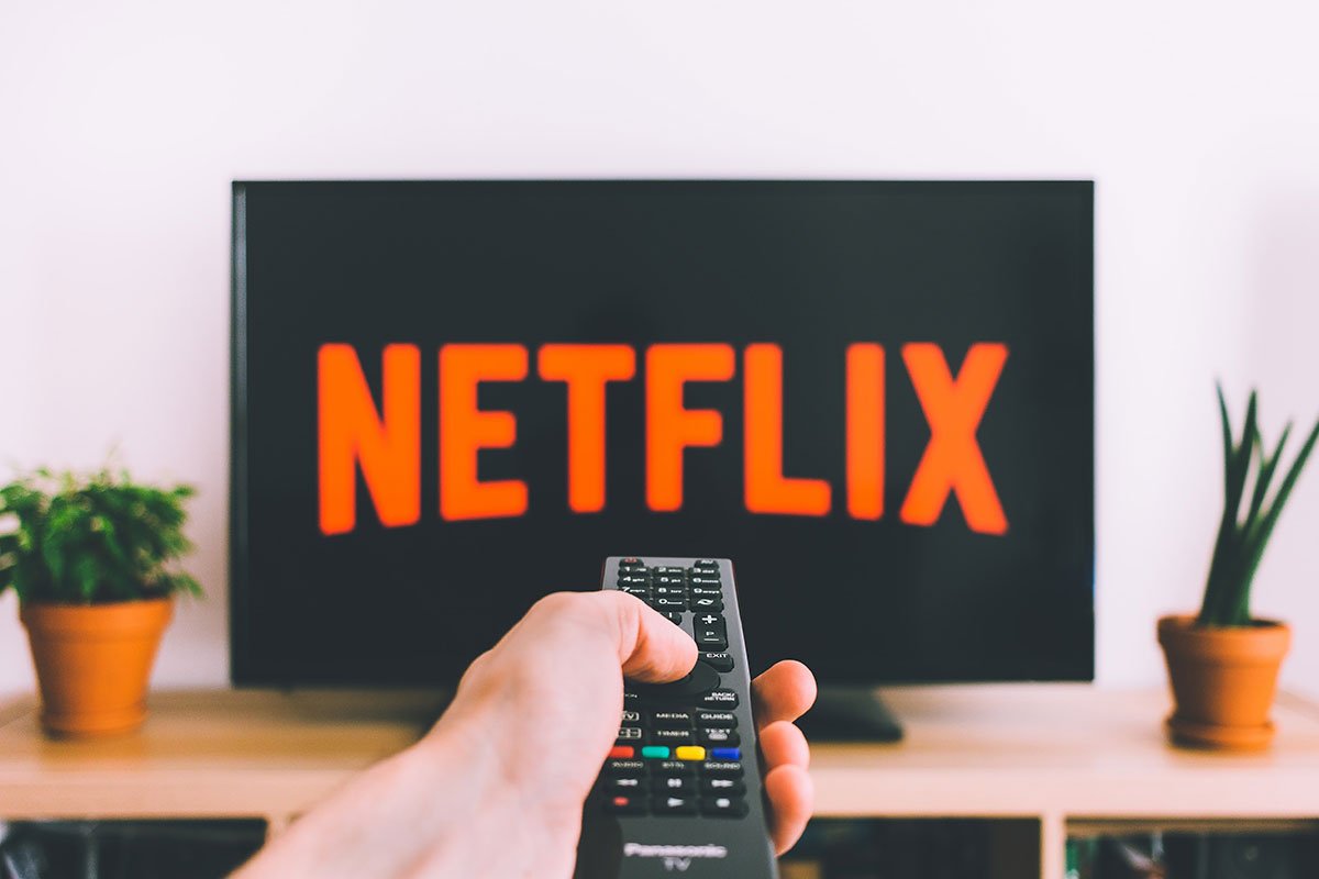 hand holding remote toward tv with netflix logo on it