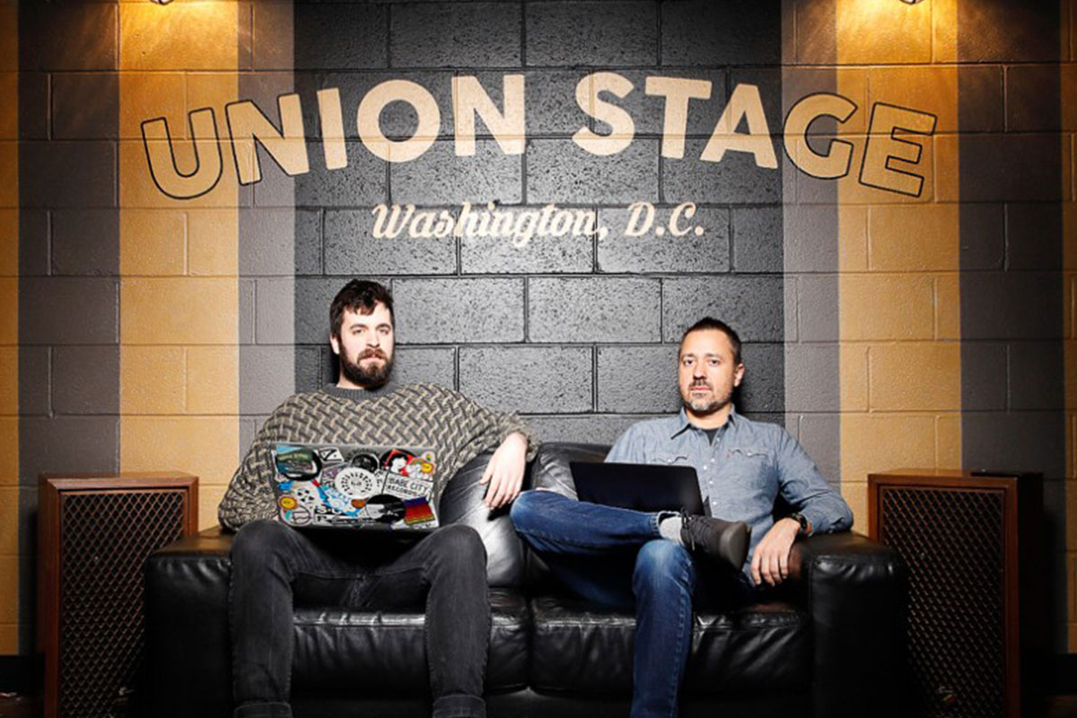 two men sitting on front of painted brick wall at union stage in washington dc