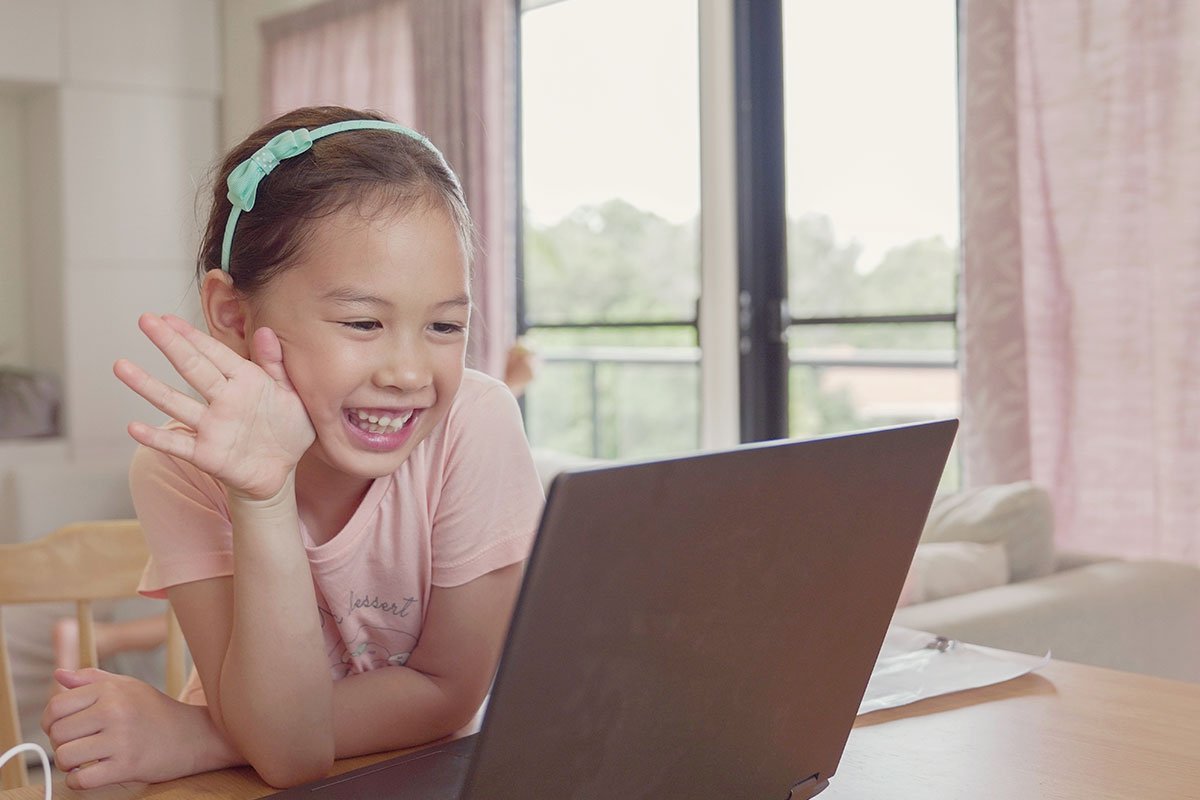 little girl waving at laptop computer with pink shirt and green headband and pink curtains