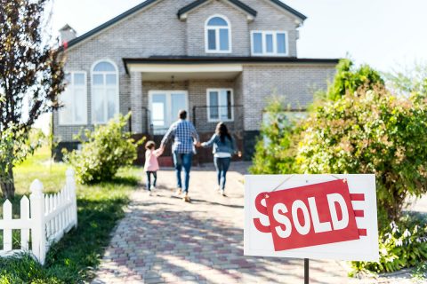 three people in a family running to a light brick home with sold sign