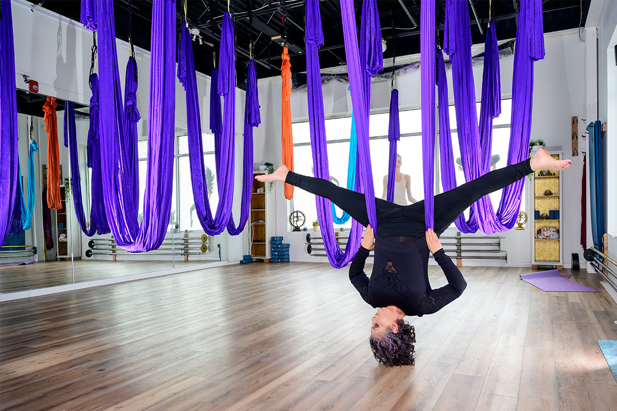 woman hanging from aerial yoga silks purple and blue in yoga studio