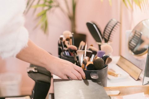 woman reaching for makeup and makeup brushes with pink and green background