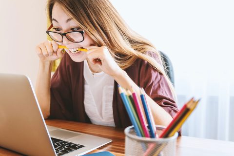 student at her desk on laptop biting pencil from stress
