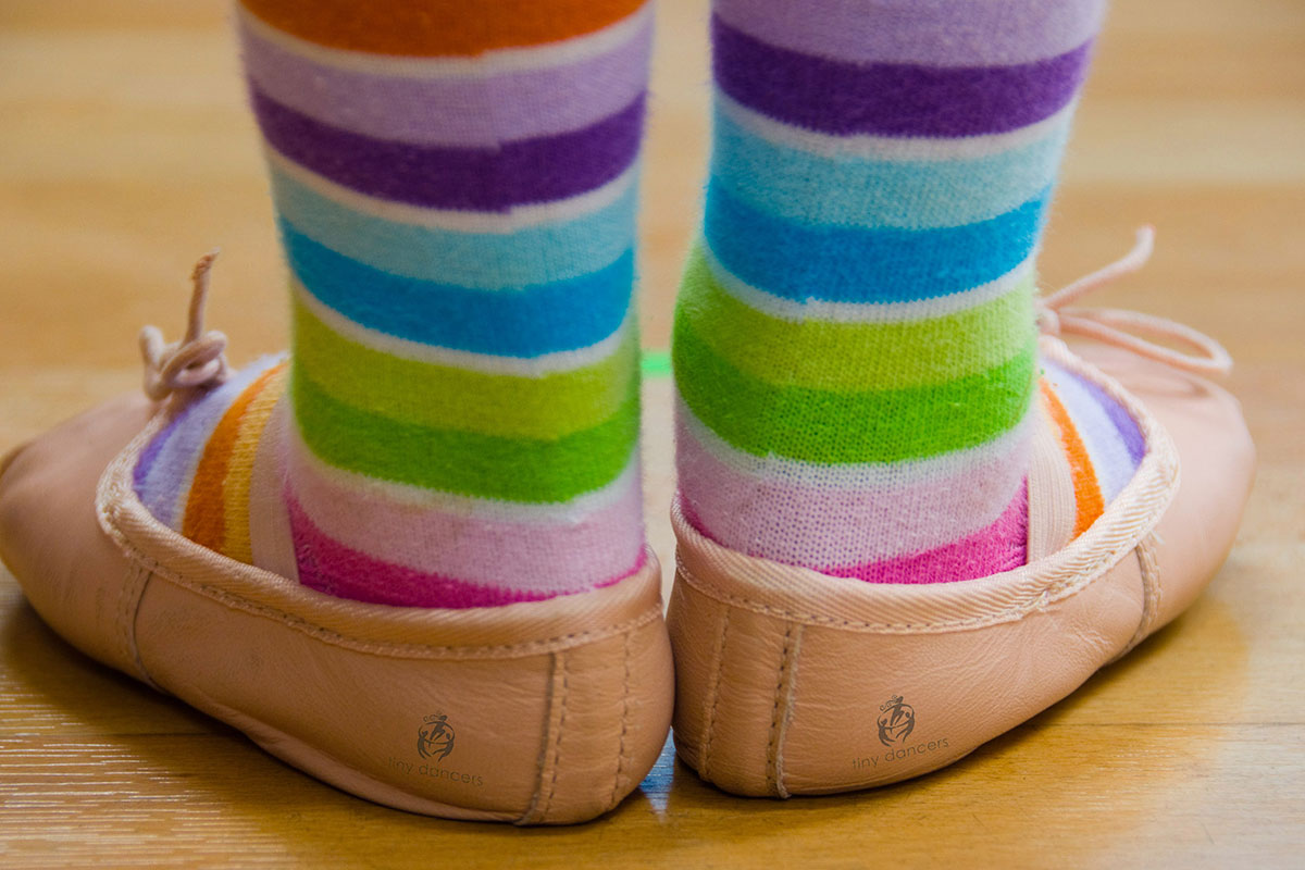 child's feet in ballet slippers with rainbow socks
