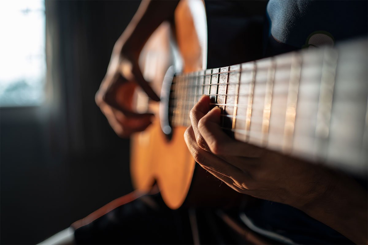person playing guitar at sunset with strings in focus