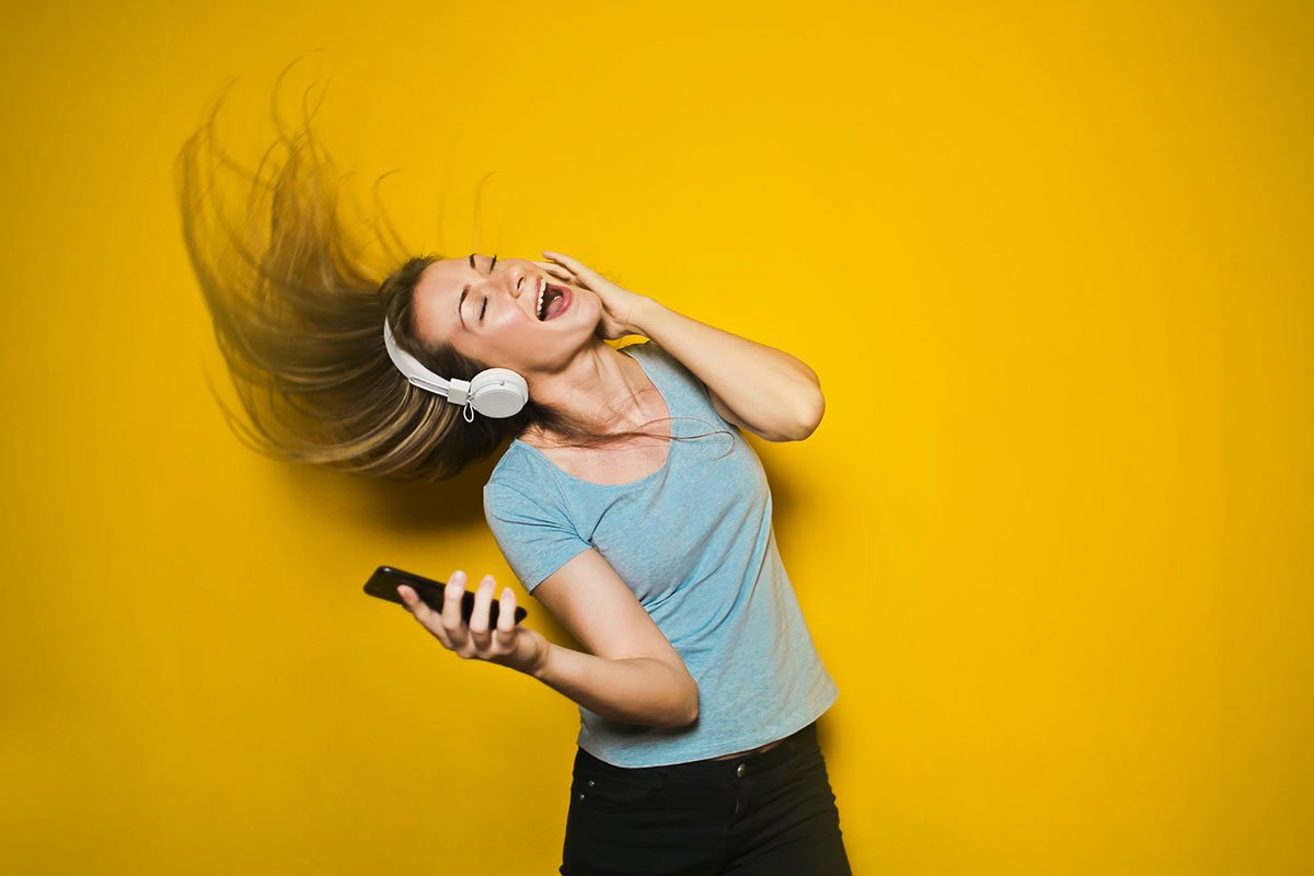woman with headphones on dancing in front of a yellow wall