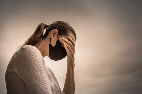 woman wearing face mask and holding head from stress