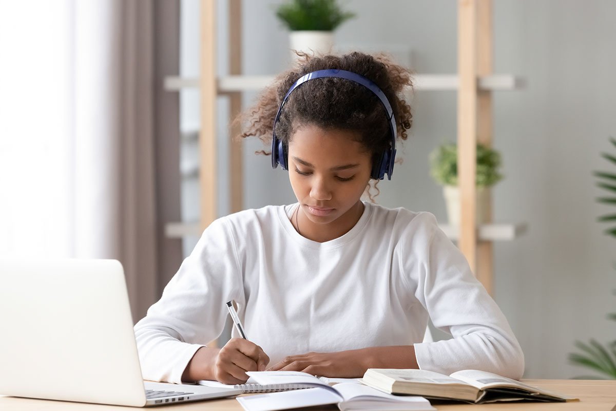 young girl in white with headphones studying at computer