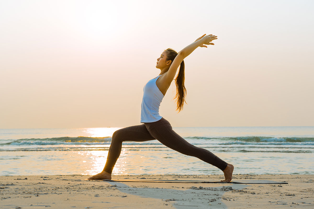 woman doing yoga on the beach with the sunrise
