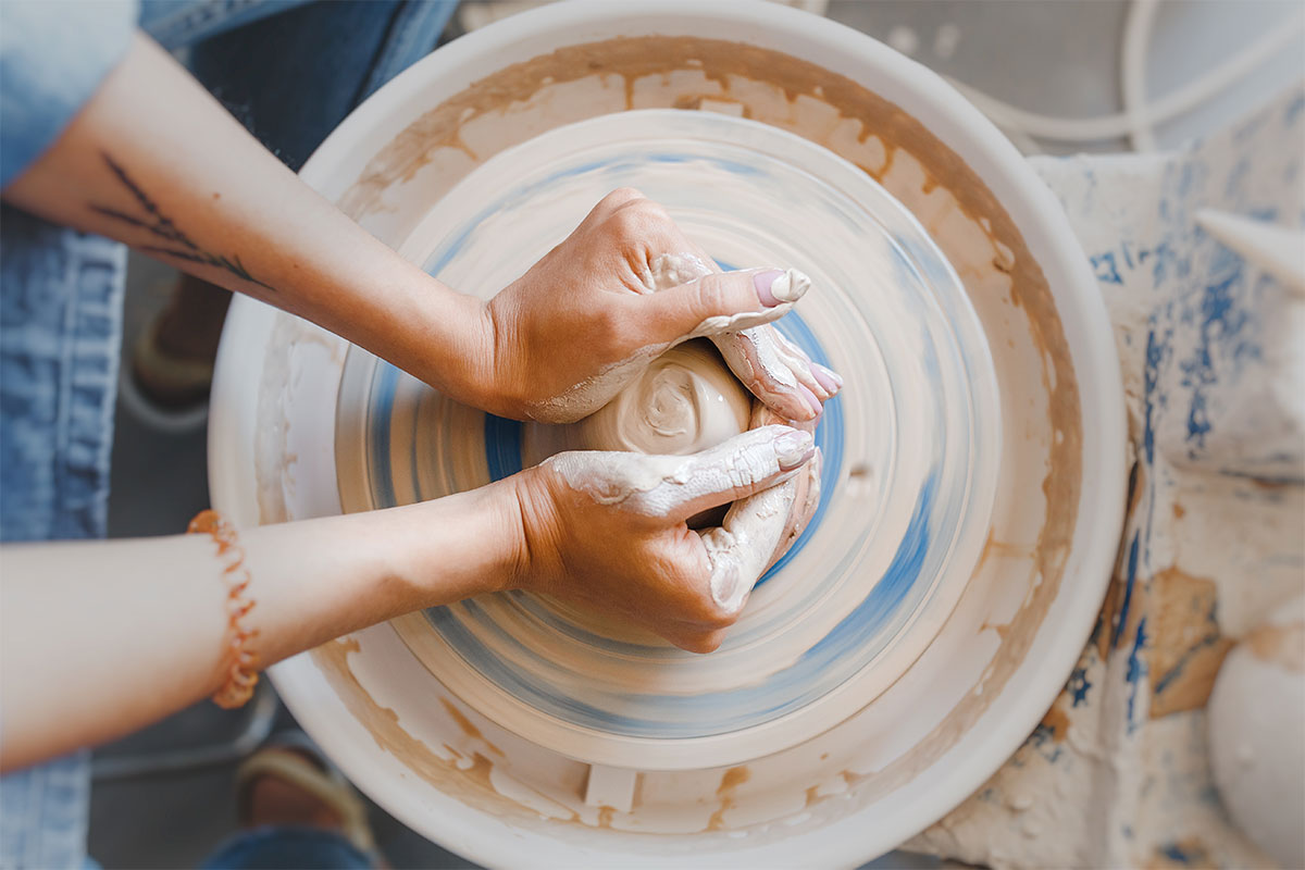 two hands on a pottery wheel with clay