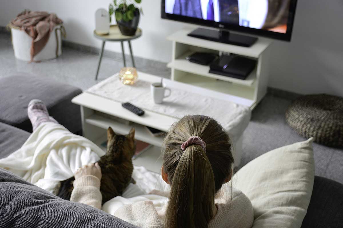 woman watching television with cat on couch