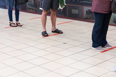social distancing with red tape on floor and people waiting in line