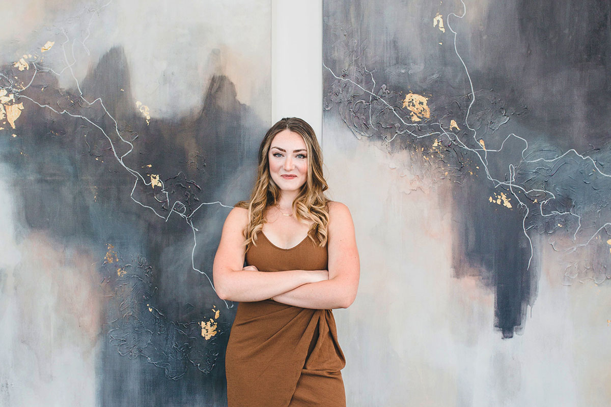 woman in brown dress in front of two abstract paintings