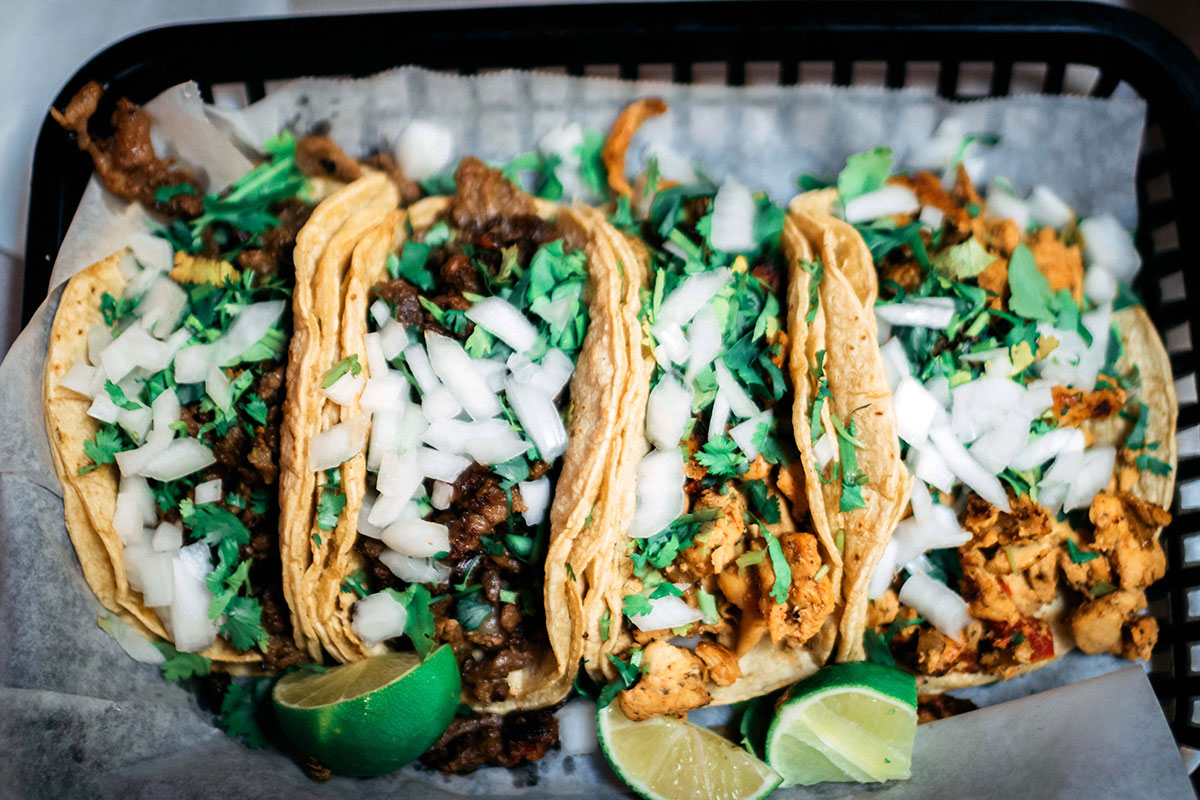 tacos in black basket with limes and onions and cilantro